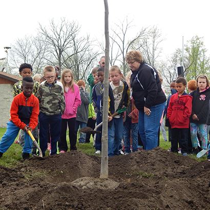 Photo of elementary school students shoveling dirt onto a newly planted tree.