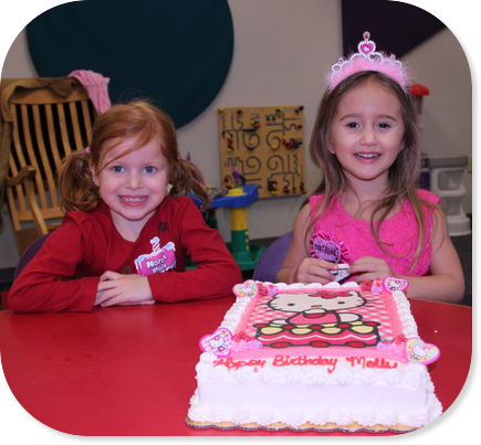 Two Girls Sitting at a Table in Front of a Birthday Cake